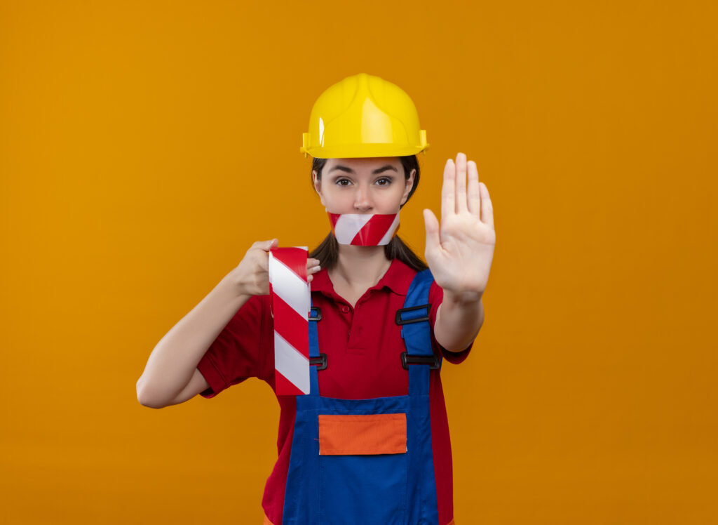 Perigo x Risco na segurança do trabalho: profissional com capacete fazendo gesto de parada e segurando fita de sinalização, representando prevenção de riscos conforme NR-1